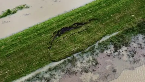 An aerial view of damage to the riverbank at Fiskerton, Lincolnshire, showing parts of it slipping away, with water from the river on both sides