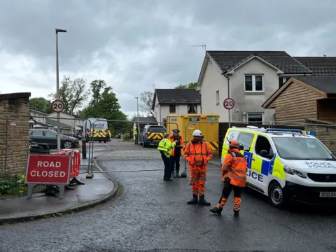 Police and workers in high-vis outside a closed-off street