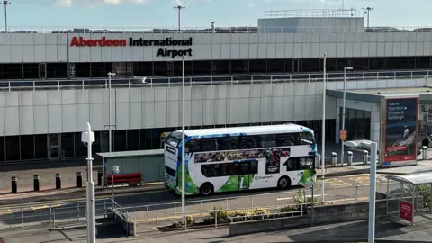 Main entrance of Aberdeen Airport. A double decker bus is on the road outside of the entrance. 