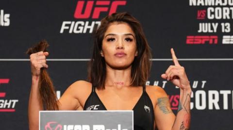 Tracy Cortez poses on the scale holding her shorn hair during the UFC weigh-in