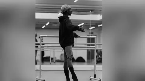 Nahum McLean/Jack Thomson Nahum in a dance studio with one foot raised and both arms wide.