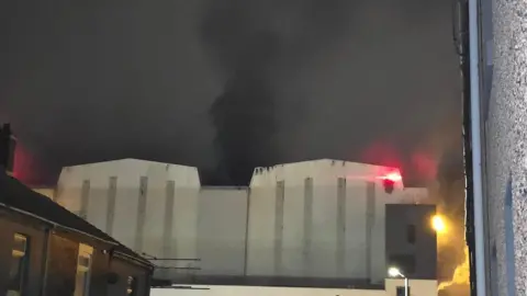 Donna Michelle Butler Smoke billows from a large white building at BAE Systems' nuclear submarine shipyard. 