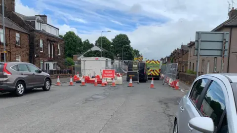 A view of the Annan Road closed with cones across it and a couple of cars parked nearby
