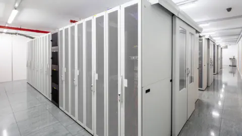 A corridor of white, mesh‑fronted server racks in a brightly lit data centre.