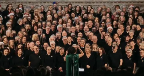 Alex Walton Photography Sam is seen wearing a green dress in front of the massed members of her choirs all wearing black 
