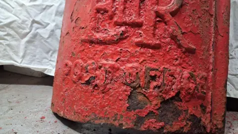 Jay Anderson Bottom of postbox with corroded red paint.