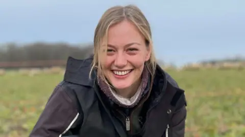 Hannah Murrell a shepherdess who is crouched down in a field with her sheepdog Roo.