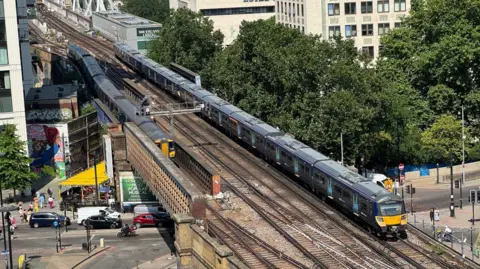Network Rail Two dark blue Southeastern trains travel on tracks on a bridge over a road which has cars and vans travelling beneath it