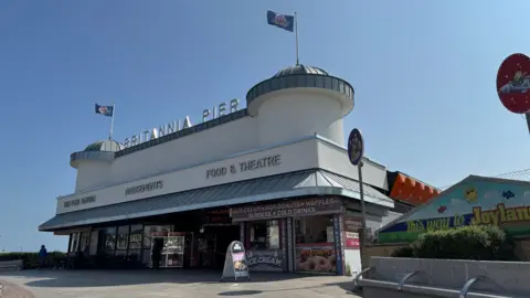 View of the new facade of Britannia Pier from the front on the right. The entrance is now white and has a sign that says Britannia Pier above the entrance.