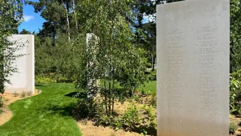 Several large stone slabs, engraved with names in a green garden setting. 