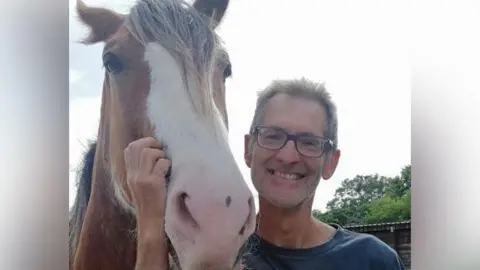 Martin Morgan smiling at the camera wearing a pair of glasses and standing next to a horse