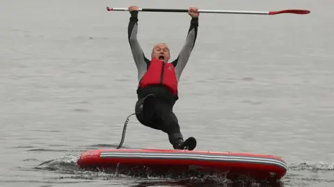 Reuters Sir Ed Davey falls off a paddleboard into a lake