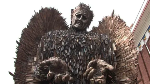 BBC The knife angel. A 27ft-tall (8m) metal sculpture in the shape of an angel with its hands held out, made from 100,000 blades.