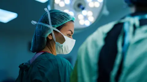 A masked female surgeon in an operating theatre