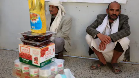 Two men sit behind food aid products