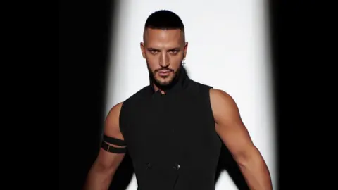 Iulia David Carl Bembridge poses in a black vest at a photoshoot