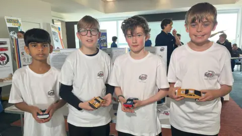 Four boys in white T-shirts holding toy cars