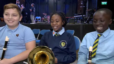 Three students involved in the project, wearing their school uniform and holding recorders as they rehearse for Symphony of the World with the Bristol Ensemble