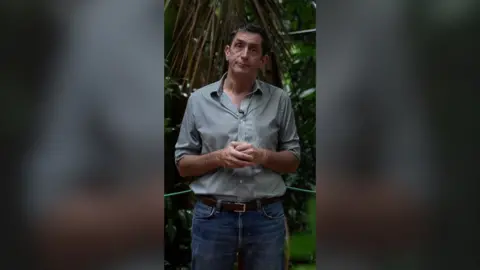 Justin Rowlatt standing in front of a forested area, looking into the camera