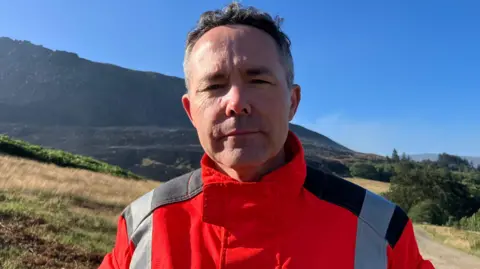 Mat Trewern/BBC Ben Levy has an orange jacked and stands in front of the moors.