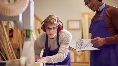 Getty Images A young carpentry student is ear protectors and safety goggles as he is shown how to work a saw