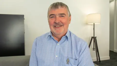 Tony Collier, wearing a blue shirt, looks straight ahead as he smiles for the camera