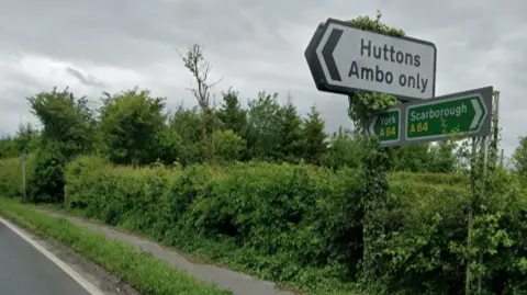 A road sign showing an arrow to turn off for Huttons Ambo, alongside directions along the A64 to York and Scarborough.