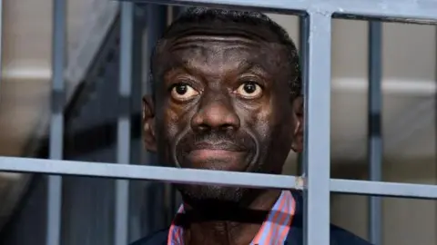 Reuters Kizza Besigye, staring ahead stands in dock behind bars at the Uganda Military General Court Martial in Kampala