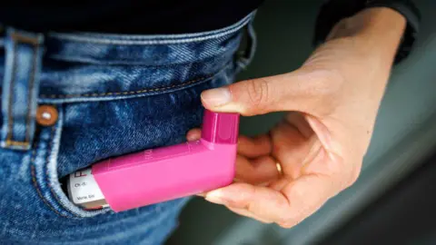A close up of a person holding a pink inhaler next to their jeans pocket