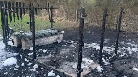 Victoria Nichols The back of the house showing where the oil tank once stood - it is surrounded by the remains of a wooden fence which has been burnt down, only blackened ashes remain. A concrete slab can be seen in the centre of the image. 