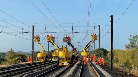 Thameslink Large yellow equipment on the railway lines providing elevated platforms for workers, dressed in orange, to reach overhead lines.