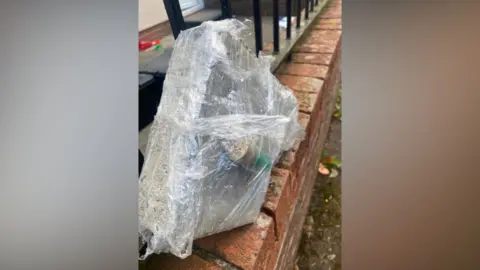 Paul McCusker What appears to be a bullet casing and a brick wrapped up in clingfilm on a wall