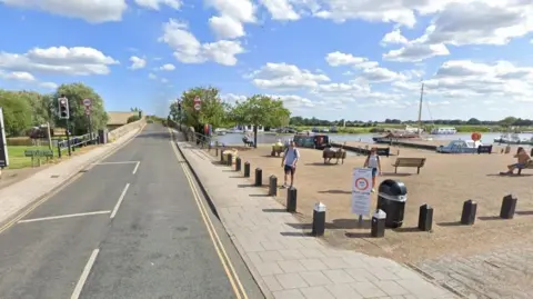 A road bridge over a river with two people walking from a small marina