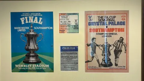 Kevin Screech A programme from the final on the left and programme from the semi final against Crystal Palace on the right. IN the middle are tickets to the games. They are all behind a picture frame.