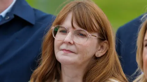 PA Archibald is pictured wearing a cream jacket and round clear glasses. She has long red hair.