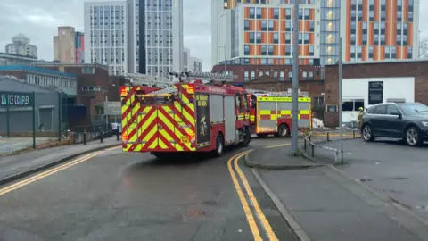 A road with yellow lines down the sides. There are two fire engines in view pictured from the back and a car to the right of the picture. 
