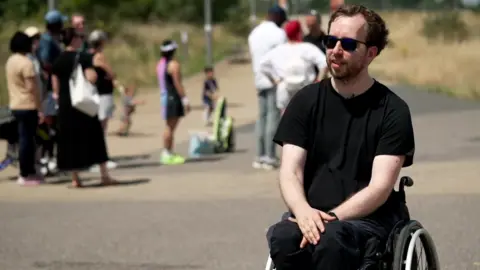 Ivan Vershigora, a man with dark hair in a black T-shirt and black trousers, wearing dark sunglasses, in a wheelchair outside