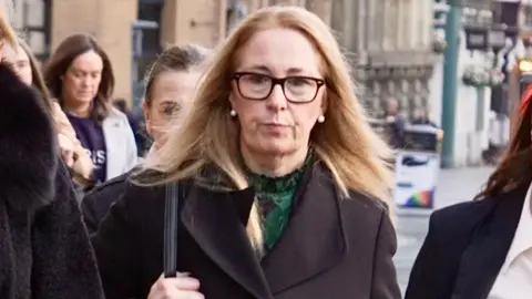 BBC Alison Kelly, who has enarthrosis  magnitude   reddish blonde hairsbreadth  and wears acheronian  rimmed glasses and a greenish  apical  nether  a achromatic  jacket, is pictured arsenic  she walks towards Liverpool Town Hall carrying a achromatic  handbag connected  her enarthrosis  and pursing her lips successful  a superior   expression