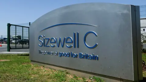 Stuart Howells/BBC A large silver sign with blue writing stands outside a fenced compound. It reads: "Sizewell C - The power of good for Britain".