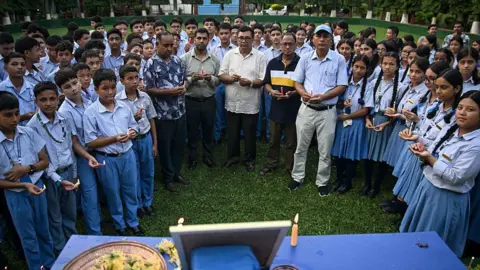 AFP via Getty Images Students and a few men hold candles and stand around a blue table