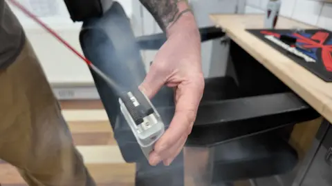 A hand holding a foil razor and spraying it with anti-bacterial spray