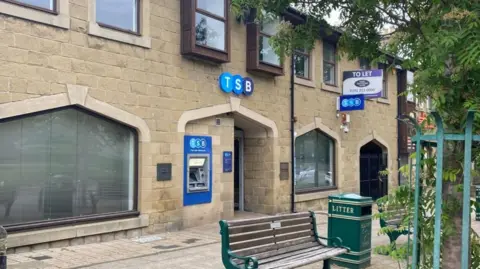 A branch of TSB with a seat and a green litter bin outside