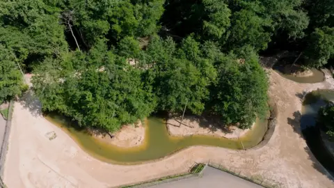 Jimmy's Farm & Wildlife Park A drone image of a reserve at a wildlife park. There are islands surrounded by a stream of water. There are large trees on the islands.