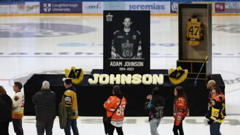 Reuters A podium with a picture of Adam Johnson next to his 47 jersey - on the ice of an ice rink 