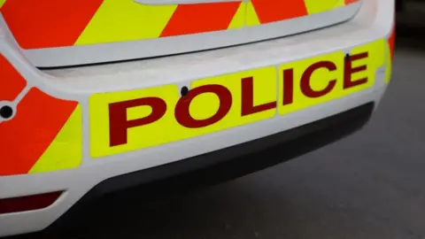 A close-up of the back of a police car which is orange and yellow. 'Police' is written across the bottom.