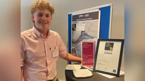 Design Innovation in Plastics Harry Wragg standing beside his national award and CPR prototypes.