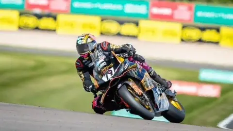 British Superbikes Championship Storm Stacey dressed all in black leather clothing on his motorbike, slanted and leaning over to one side, with his knee almost skimming the ground. His race number 79 clearly visible of the front of his bike