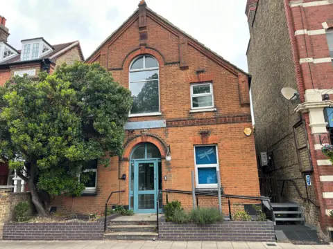 A nursery, a red brick building with a sign outside and a green tree 