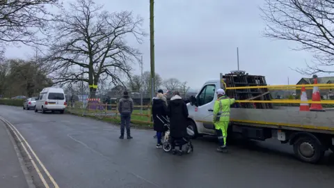 Cathy Killick/BBC A cluster of people stand next to a trailer with their backs to the camera. They appear to be looking at a tree.