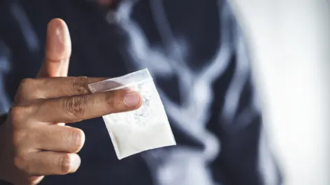 Getty Images Man holding a bag of white powder in his hand.